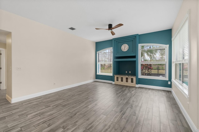 unfurnished living room with wood finished floors, ceiling fan, healthy amount of natural light, and baseboards
