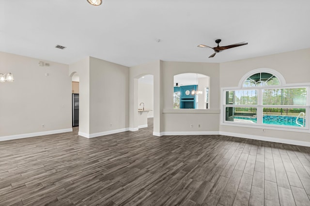 unfurnished living room with dark wood-type flooring, ceiling fan, baseboards, and arched walkways