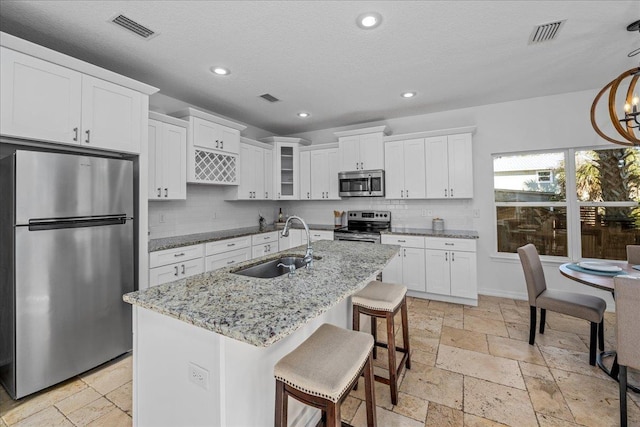 kitchen featuring sink, white cabinetry, stainless steel appliances, light stone counters, and an island with sink