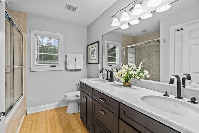 full bathroom with combined bath / shower with glass door, vanity, a textured ceiling, hardwood / wood-style floors, and toilet