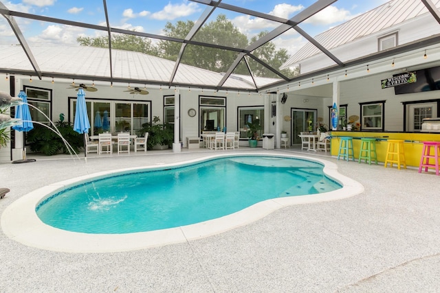 view of pool featuring exterior bar, pool water feature, ceiling fan, a lanai, and a patio area