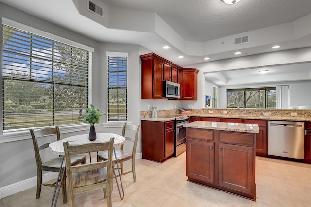 kitchen featuring stainless steel appliances, a raised ceiling, light stone countertops, and light tile patterned flooring