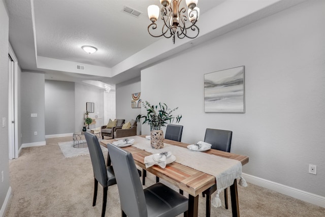 dining room with light carpet, a textured ceiling, a raised ceiling, and a chandelier