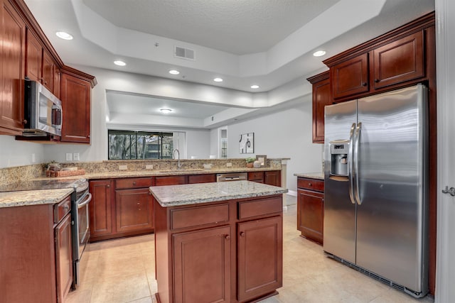 kitchen with sink, light stone counters, a center island, appliances with stainless steel finishes, and a raised ceiling