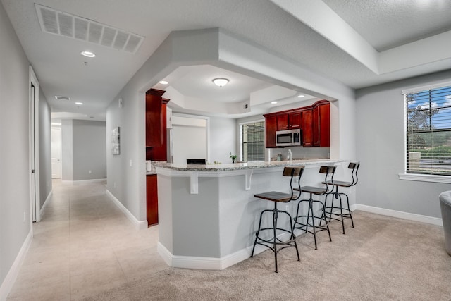 kitchen with sink, a kitchen breakfast bar, a tray ceiling, light colored carpet, and kitchen peninsula