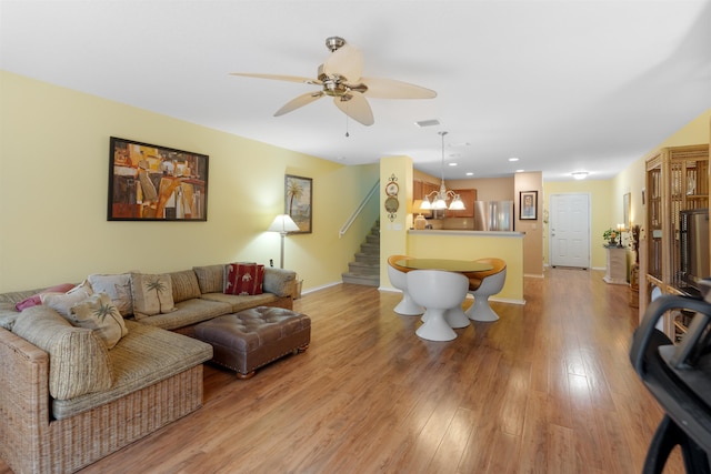 living room with ceiling fan with notable chandelier and light hardwood / wood-style floors