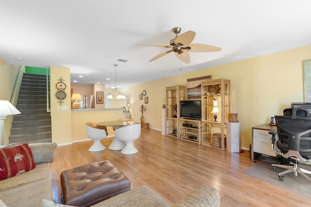 living room with ceiling fan with notable chandelier and light wood-type flooring