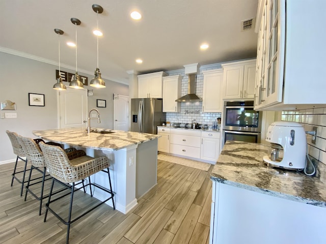 118 Sierras Loop, Saint Augustine, FL 32086 - kitchen featuring appliances with stainless steel finishes, ornamental molding, wall chimney exhaust hood, light wood finished floors, and tasteful backsplash