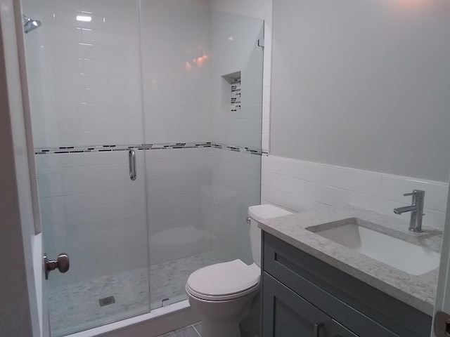 bathroom featuring vanity, toilet, tile walls, and a shower with door