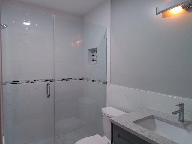 bathroom featuring toilet, vanity, an enclosed shower, and tile walls