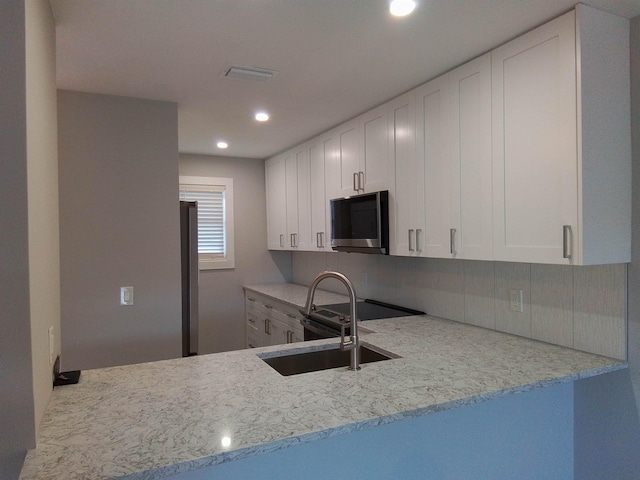 kitchen featuring kitchen peninsula, white cabinetry, light stone countertops, electric stove, and decorative backsplash