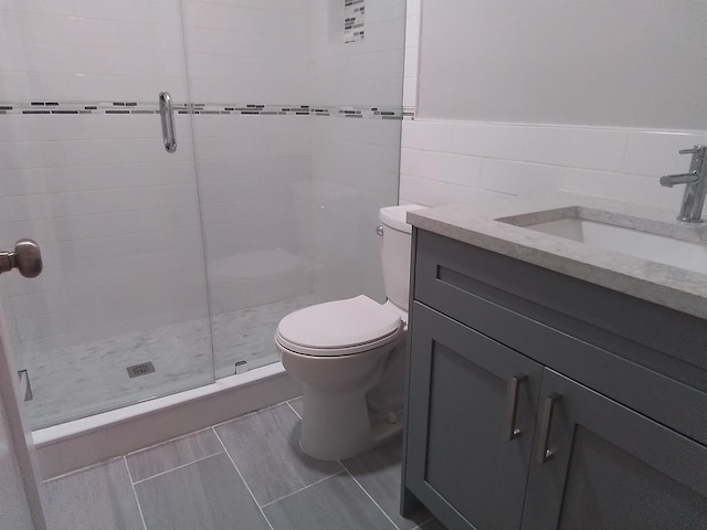 bathroom with tile walls, toilet, vanity, and an enclosed shower