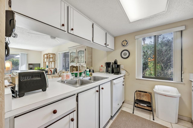 kitchen featuring sink, light tile patterned floors, dishwasher, a textured ceiling, and white cabinets