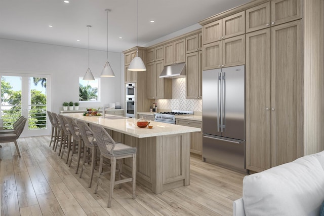 kitchen featuring light wood-type flooring, decorative light fixtures, a center island with sink, and high quality appliances