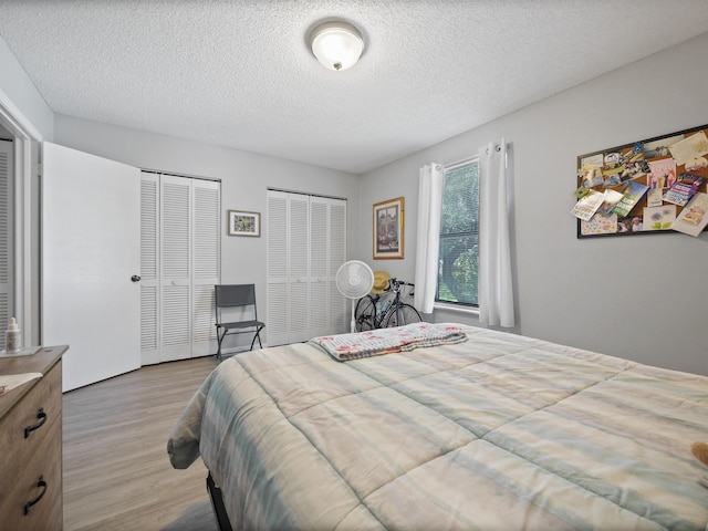 bedroom with multiple closets, a textured ceiling, and light hardwood / wood-style flooring