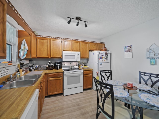 kitchen with rail lighting, a textured ceiling, white appliances, sink, and light hardwood / wood-style floors