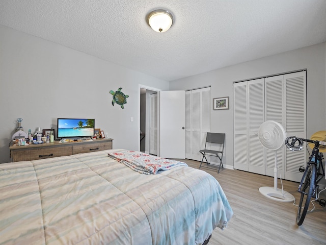 bedroom featuring multiple closets, light hardwood / wood-style flooring, and a textured ceiling