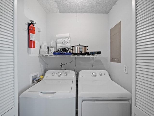 washroom featuring washing machine and clothes dryer, electric panel, and a textured ceiling