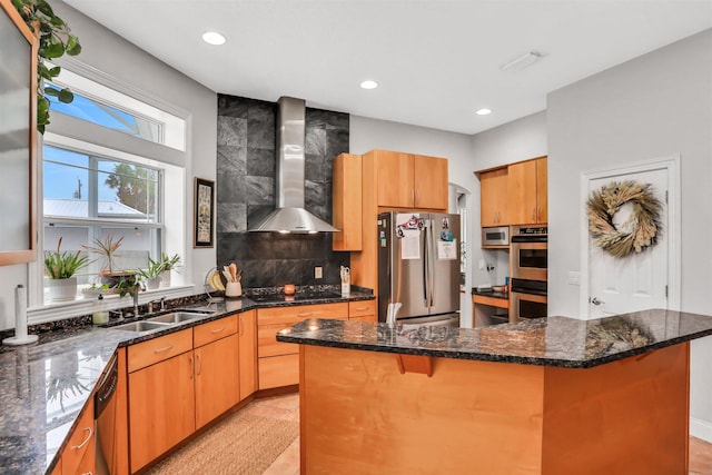 kitchen featuring wall chimney exhaust hood, dark stone countertops, sink, and appliances with stainless steel finishes