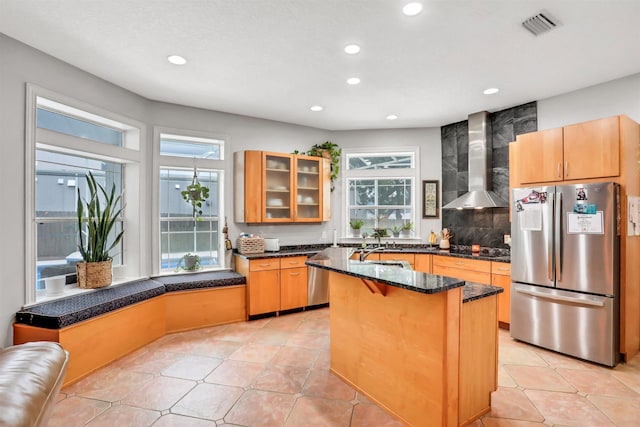 kitchen featuring decorative backsplash, a kitchen breakfast bar, stainless steel appliances, wall chimney range hood, and an island with sink