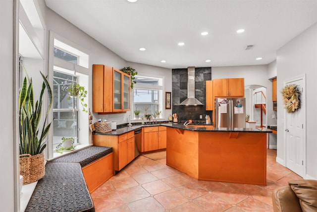 kitchen featuring a center island, wall chimney range hood, a healthy amount of sunlight, and appliances with stainless steel finishes