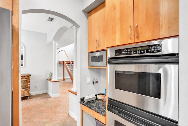 kitchen featuring appliances with stainless steel finishes, ornate columns, dark stone counters, and light tile patterned flooring