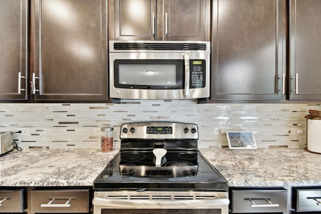 kitchen with appliances with stainless steel finishes, tasteful backsplash, light stone counters, and dark brown cabinets