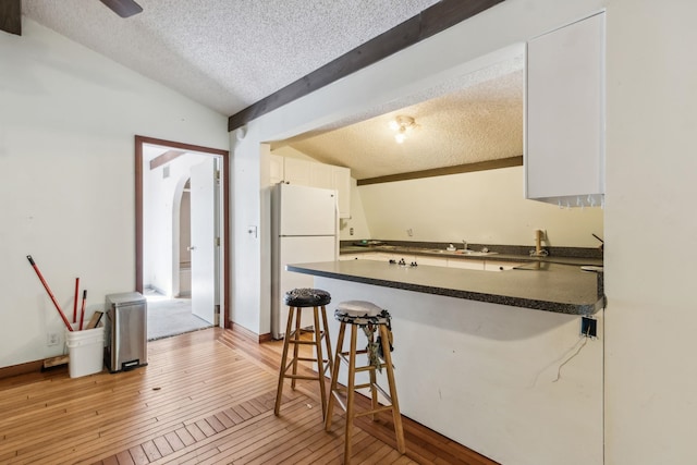 kitchen with white refrigerator, light hardwood / wood-style floors, a textured ceiling, a breakfast bar, and white cabinets