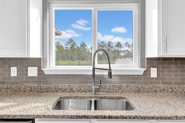 room details featuring light stone countertops, tasteful backsplash, white cabinetry, and sink