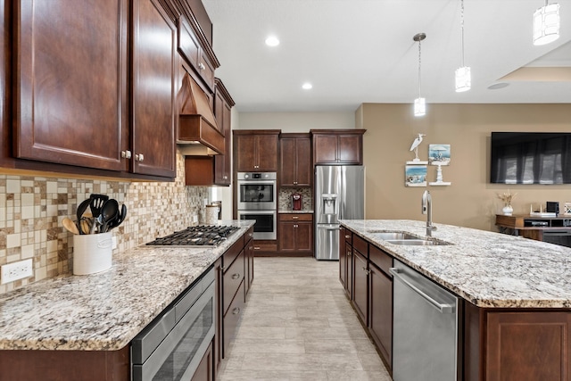 kitchen featuring backsplash, a center island with sink, sink, appliances with stainless steel finishes, and decorative light fixtures