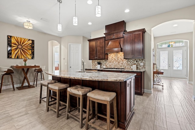 kitchen with a kitchen island with sink, sink, pendant lighting, and custom range hood