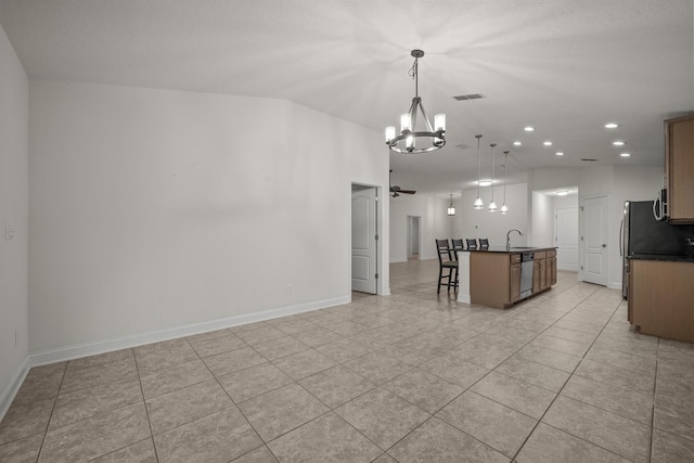 kitchen with a sink, appliances with stainless steel finishes, dark countertops, a kitchen breakfast bar, and a notable chandelier