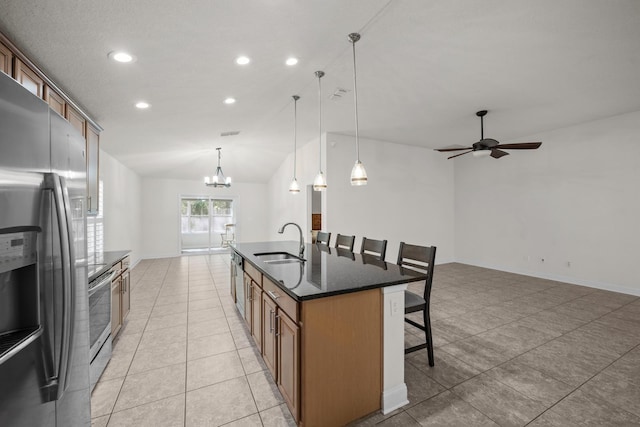 kitchen with a kitchen bar, a kitchen island with sink, a sink, stainless steel appliances, and brown cabinetry