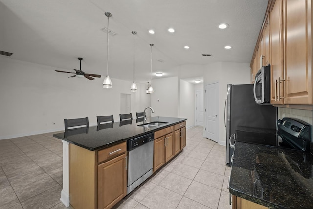 kitchen with a kitchen island with sink, a sink, dark stone countertops, stainless steel appliances, and light tile patterned floors