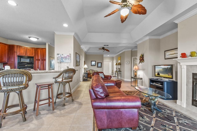 tiled living room featuring a raised ceiling, a tiled fireplace, crown molding, and a textured ceiling