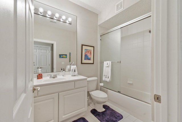 full bathroom featuring vanity, tile patterned floors, bath / shower combo with glass door, toilet, and a textured ceiling