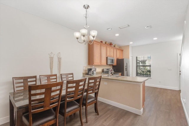 kitchen featuring stainless steel appliances, light hardwood / wood-style flooring, kitchen peninsula, pendant lighting, and light brown cabinetry