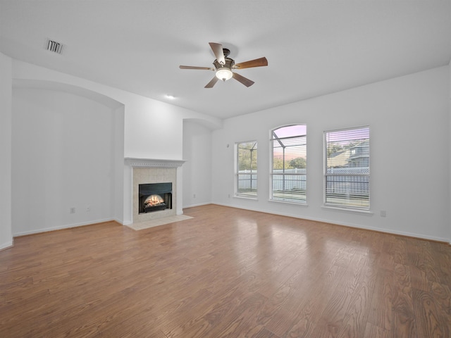 unfurnished living room with visible vents, a tiled fireplace, a ceiling fan, wood finished floors, and baseboards