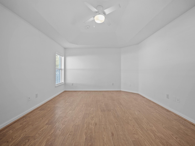 unfurnished room with light wood finished floors, a raised ceiling, a ceiling fan, and baseboards