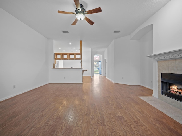 unfurnished living room with visible vents, a tiled fireplace, light wood-style flooring, and baseboards