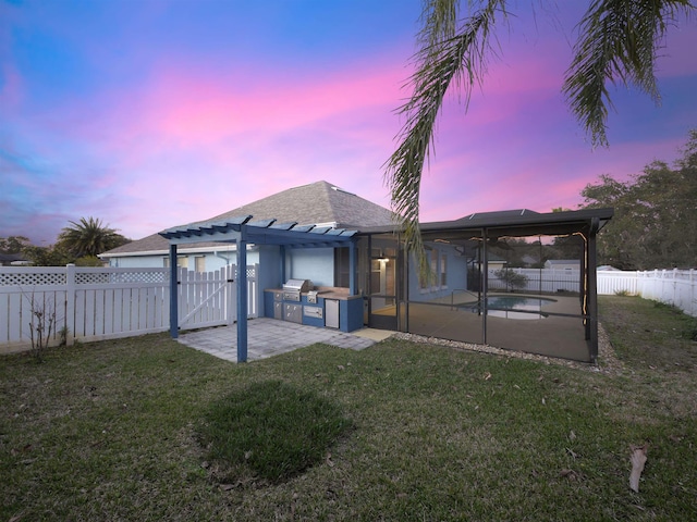 back of house at dusk featuring a patio area, a fenced backyard, exterior kitchen, and a yard