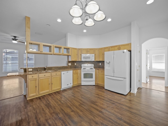 kitchen featuring arched walkways, light stone counters, a peninsula, white appliances, and a sink