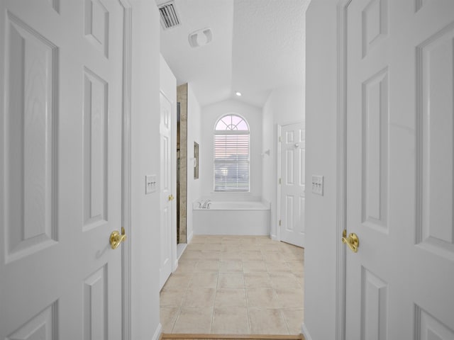 hall with lofted ceiling, light tile patterned floors, visible vents, and a textured ceiling