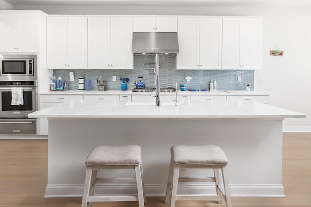 kitchen featuring an island with sink, appliances with stainless steel finishes, and white cabinets