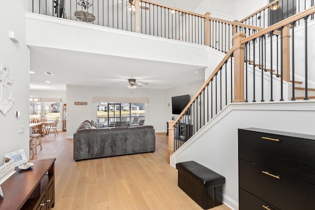 living room with ceiling fan with notable chandelier, a towering ceiling, and light hardwood / wood-style floors