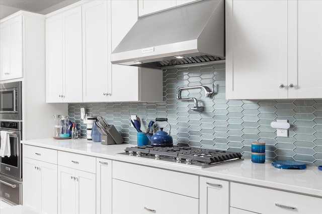 kitchen with range hood, tasteful backsplash, white cabinets, light stone counters, and stainless steel appliances