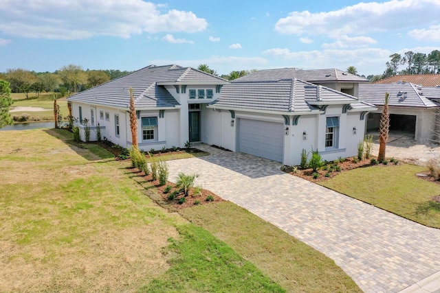 view of front of property with a garage, a tile roof, stucco siding, a front lawn, and decorative driveway