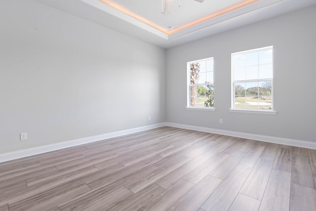 spare room with a tray ceiling, baseboards, light wood finished floors, and a ceiling fan