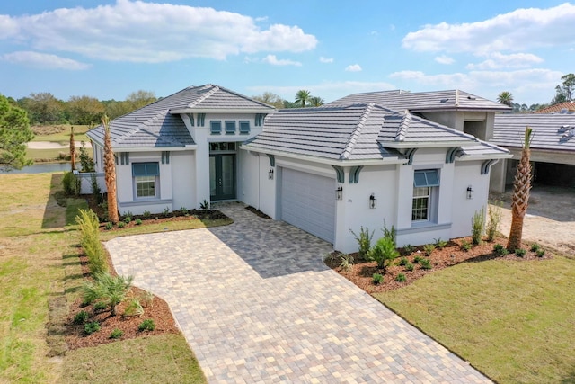 view of front of property with a tiled roof, stucco siding, decorative driveway, a front lawn, and a garage