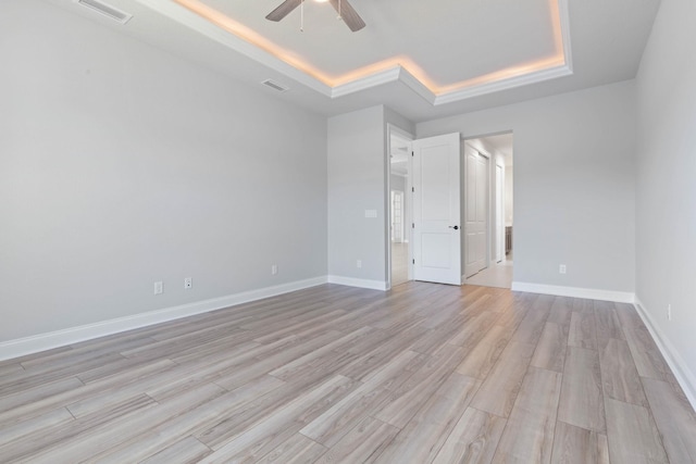 spare room with baseboards, a ceiling fan, visible vents, a raised ceiling, and light wood finished floors